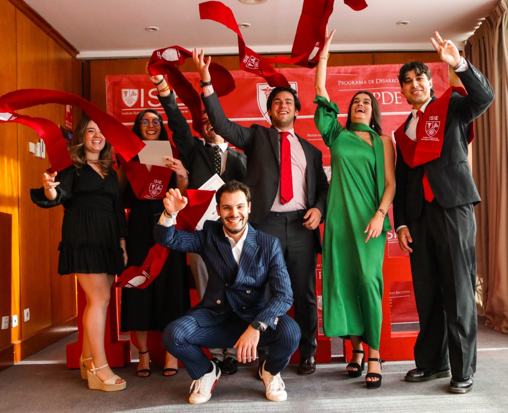 Imagen de siete alumnos graduados con las becas de ISIE. Cuatro hombres y tres mujeres vestidos de manera elegante y felices levantando su beca.